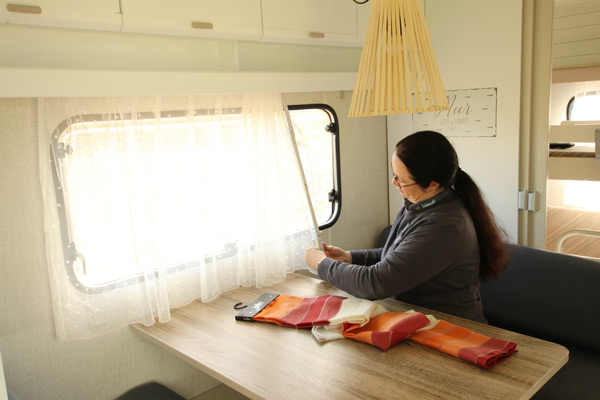 Weißer Vorhang wird von einer Mitarbeiterin vor einem Fenster von einem Camper maßgeschneidert.