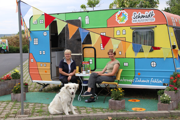 Vor dem neu renoviertem Camper sitzen Frau Schmidt, ihr Hund und eine weitere Frau.
