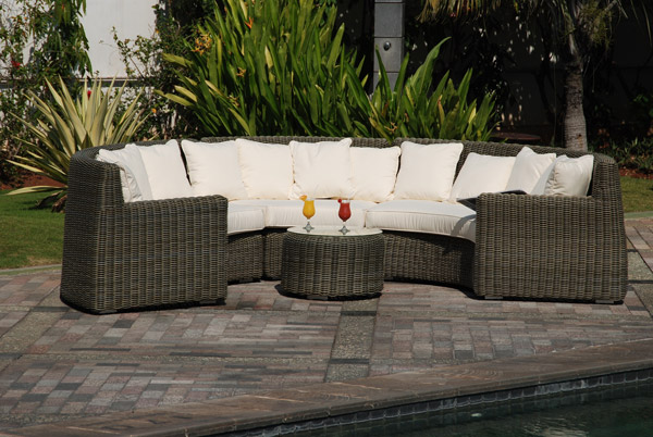 Schickes halbrundes Gartensofa, mit Tischchen in der Mitte, auf einer Terrasse.