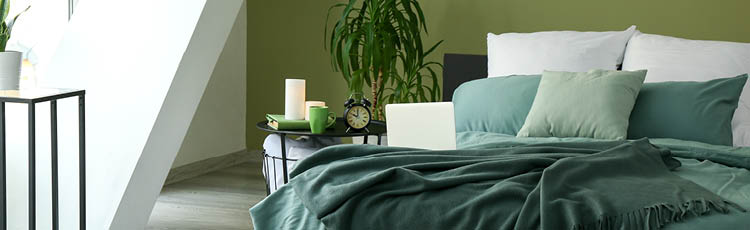 Bett in ruhigem Dunkelgrün mit Bettwäsche aus Naturfasern. 