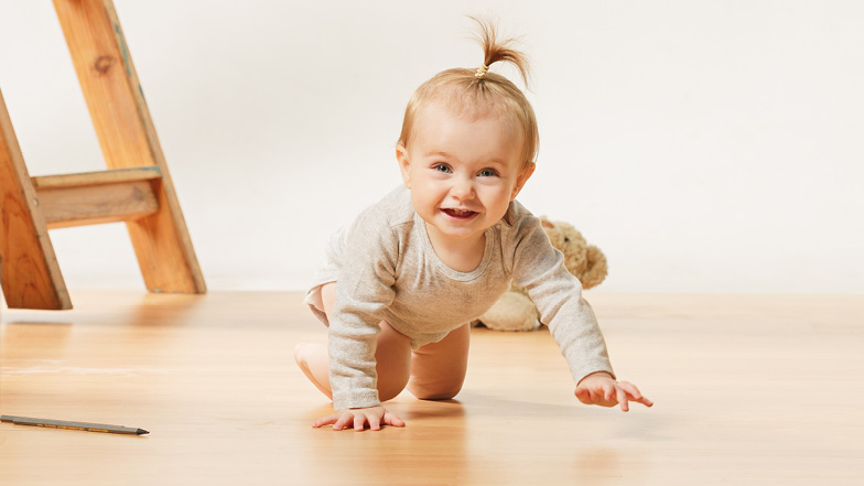 Baby krabbelt auf warmen Holzboden